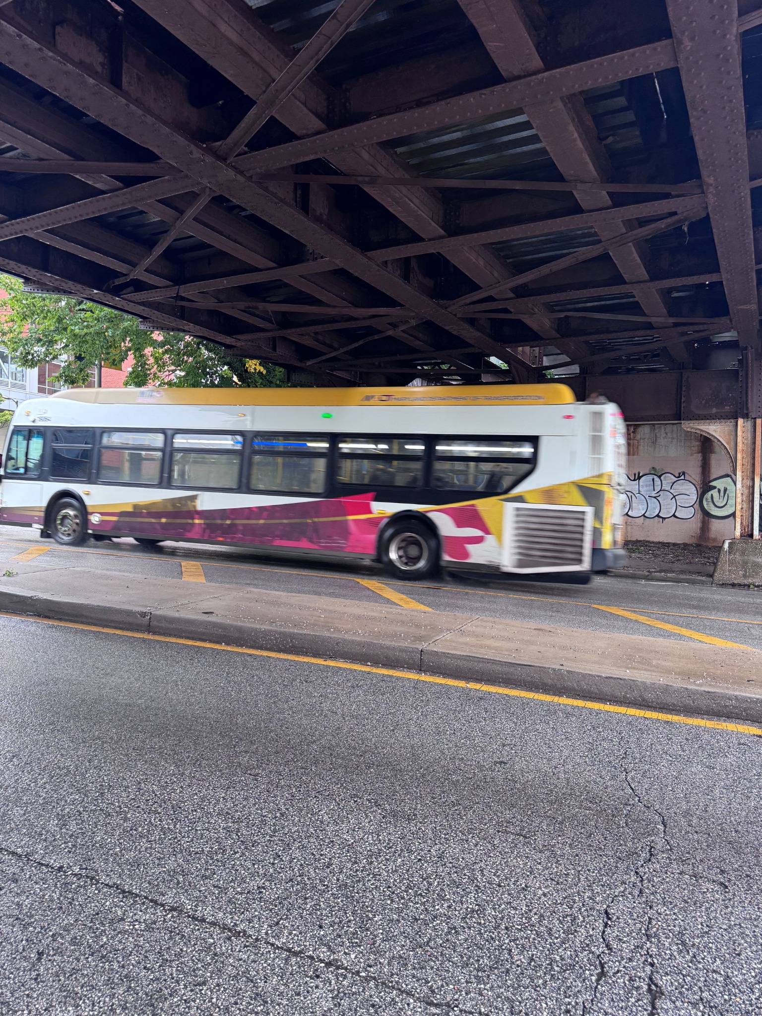 Yellow and burgundy bus passing beneath the bridge